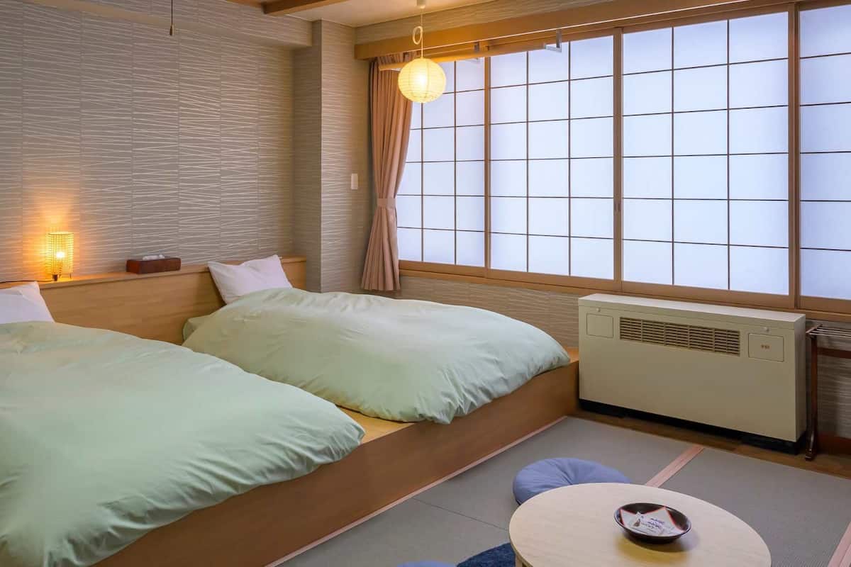 A room with a bed, a table, a heater, and a window with a view.