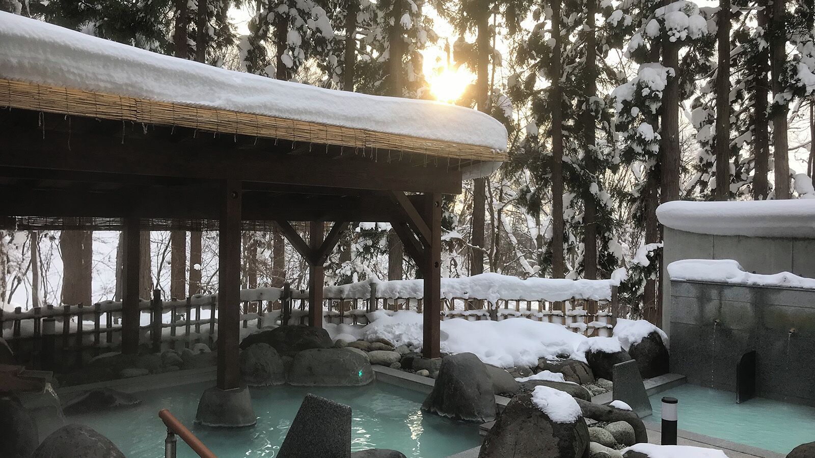 A traditional Japanese onsen with a wooden structure, a stone bath, and a surrounding snowy landscape.