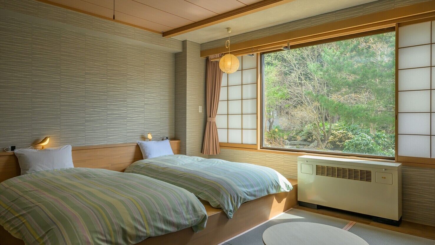 A traditional Japanese-style bedroom with tatami flooring, a futon bed, a shoji screen, and a view of a forest.