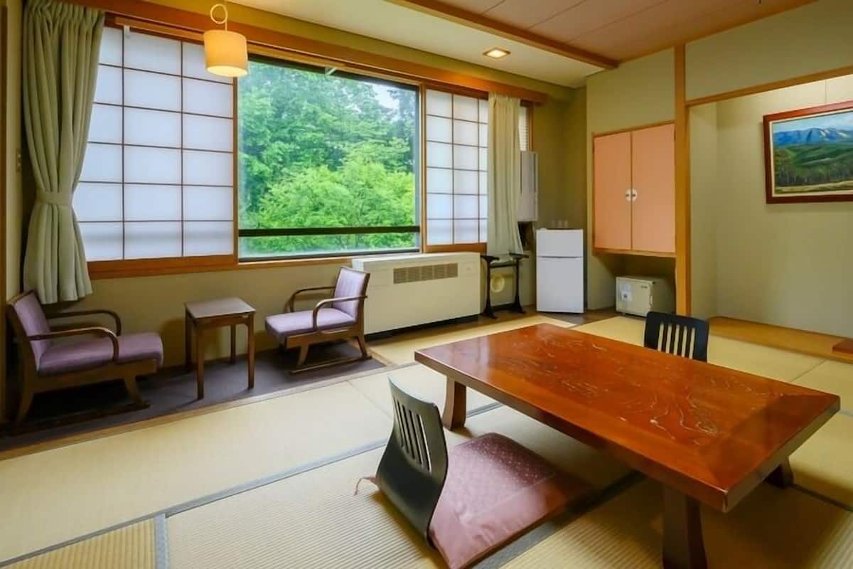 A traditional Japanese-style room with tatami flooring, a low table, and a view of greenery outside.