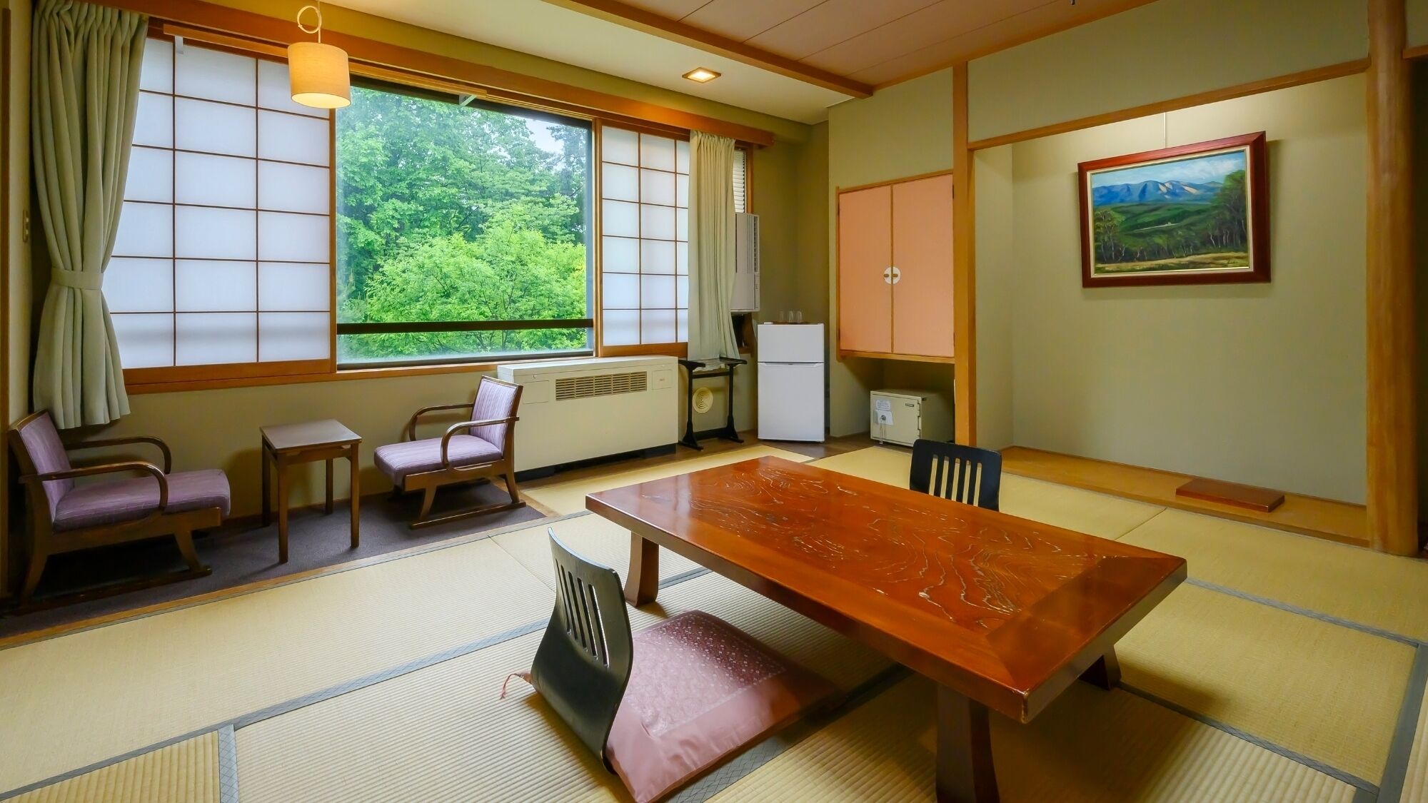 A traditional Japanese room with tatami flooring, a low table, chairs, a radiator, and a painting on the wall.
