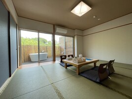 Una habitación con tatami, puerta corredera de cristal que da a un jardín, una mesa de madera y un inodoro de estilo japonés tradicional.