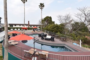 Un área de piscina con sillas de descanso y sombrillas, rodeada de palmeras y un edificio al fondo.