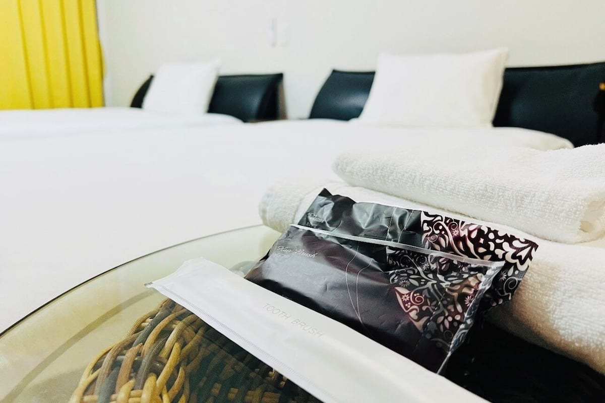 A hotel room with a bed, pillows, a glass table with a toothbrush and toothpaste, and a towel.