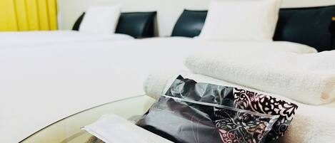 Habitación de hotel con cama, almohadas, una mesita con cepillo e pasta de dientes, y una toalla.