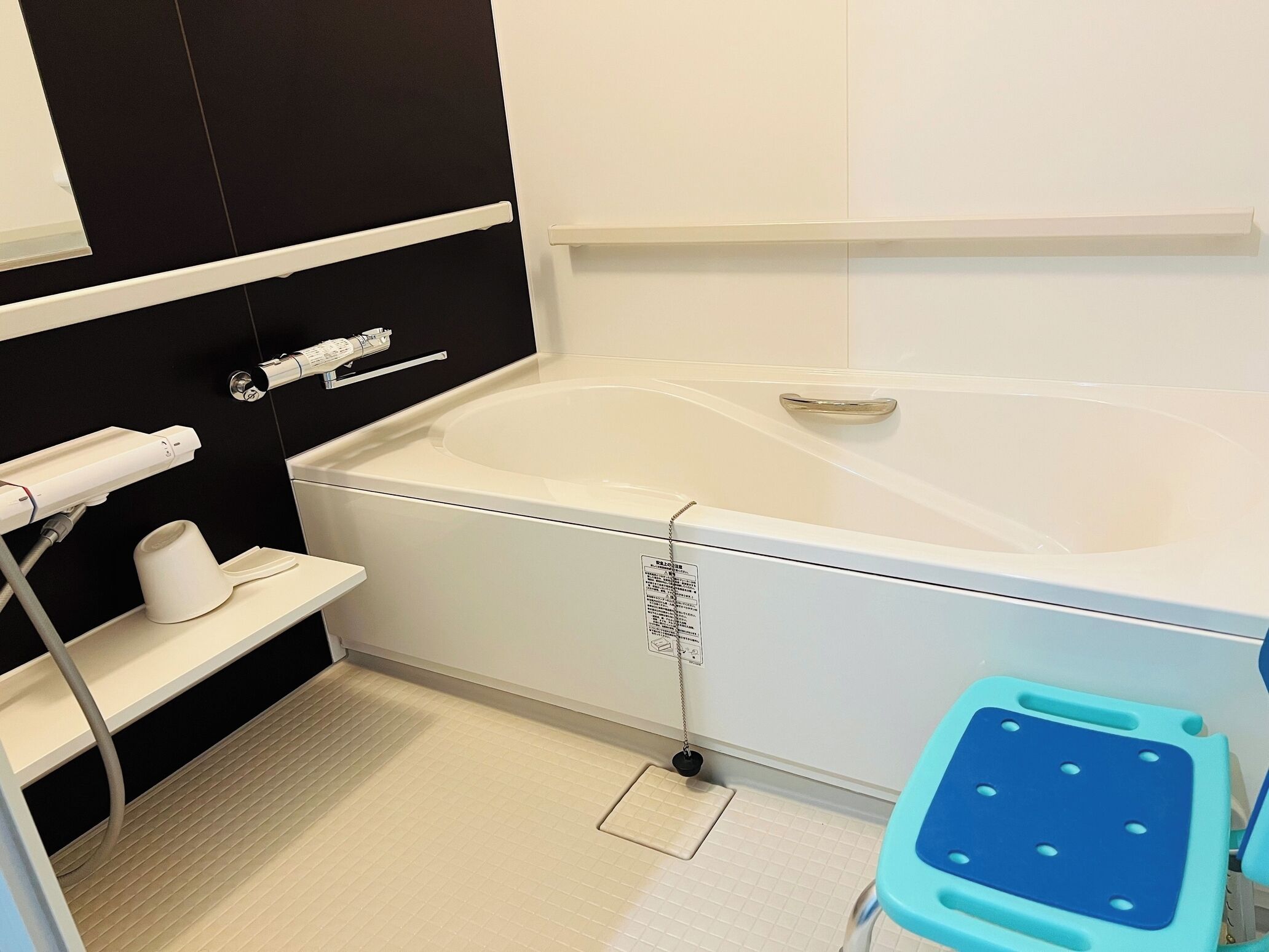 A modern bathroom with a bathtub, a towel rack, a toilet paper holder, and a blue stool.