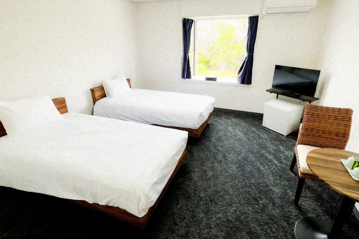 A hotel room with two beds, a TV, a desk, and a window with curtains.