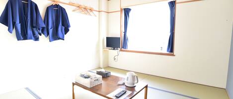 A traditional Japanese room with tatami flooring, a low wooden table with a kettle and remote, and a TV on a stand.
