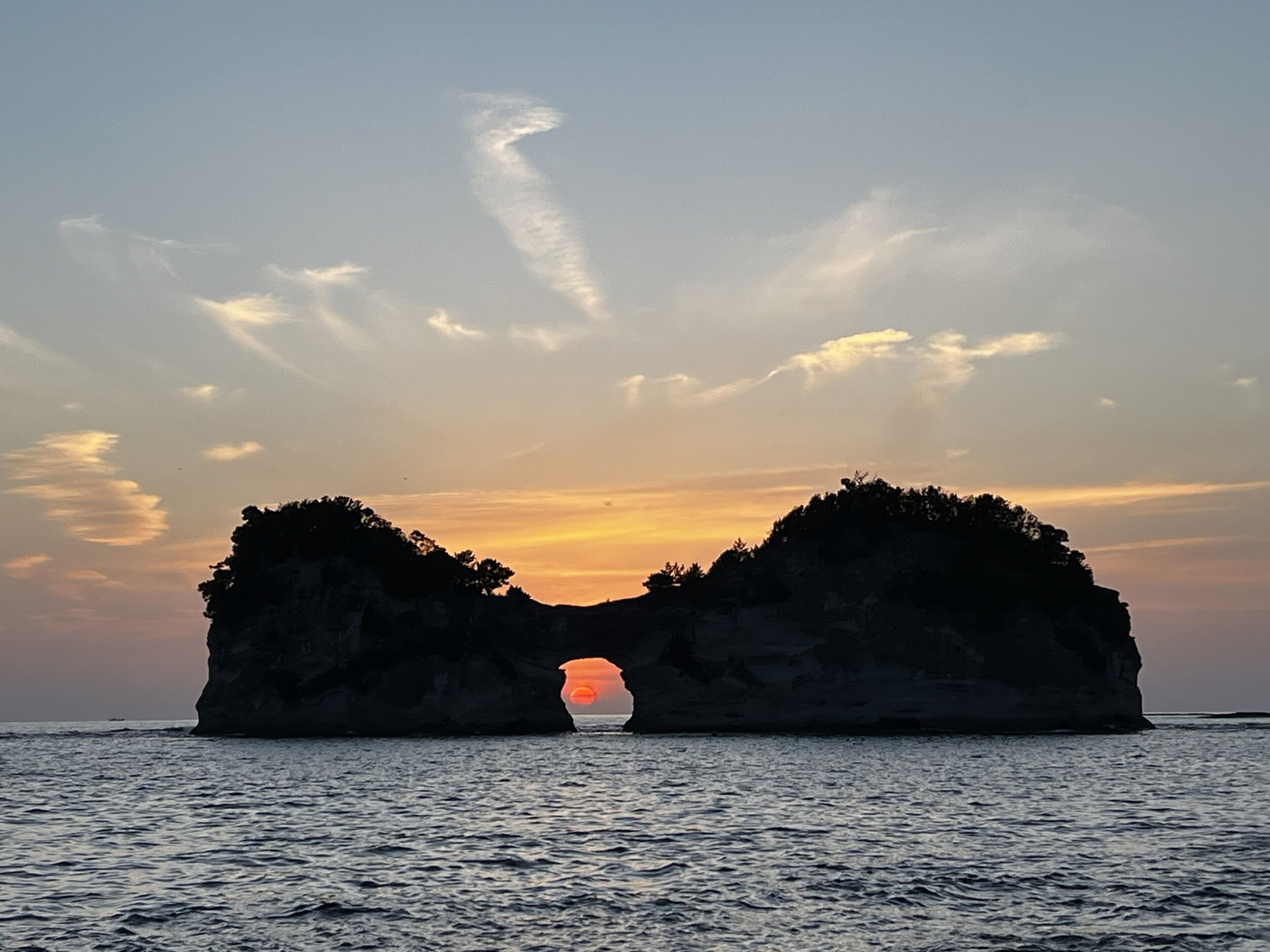 A sunset over a rock formation with a natural archway.