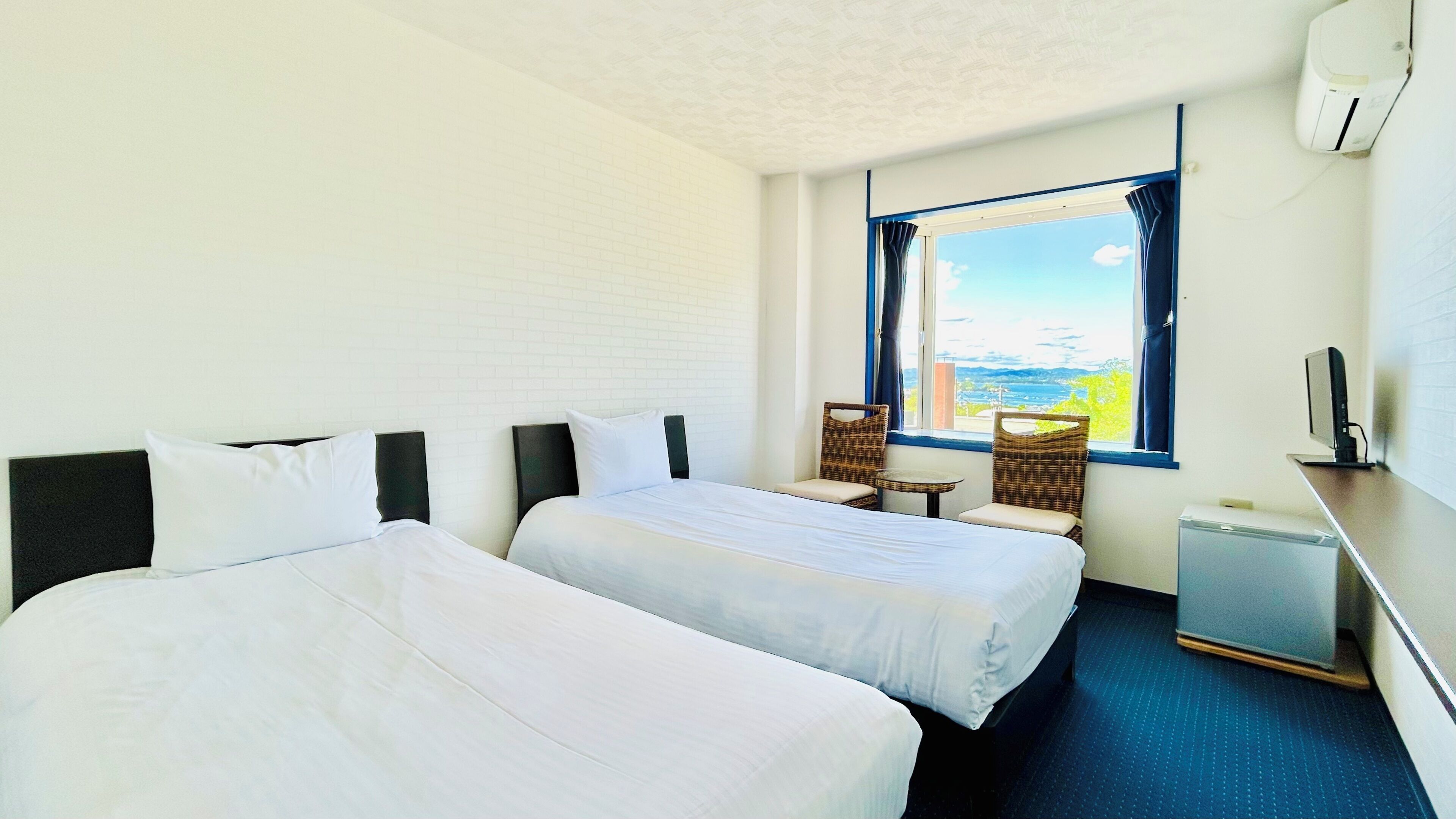 Habitación de hotel con dos camas, una mesita, sillas, televisión y ventana con vistas.