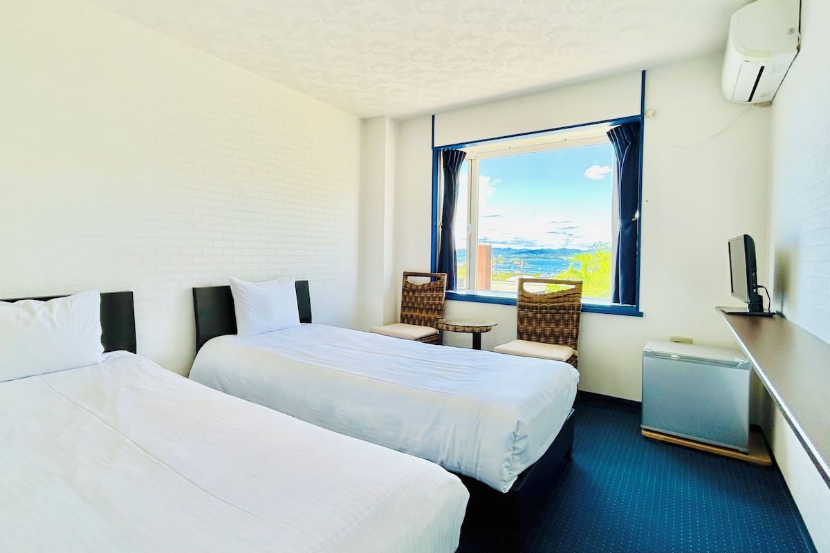 Habitación de hotel con dos camas, una mesita, sillas, televisión y ventana con vistas.