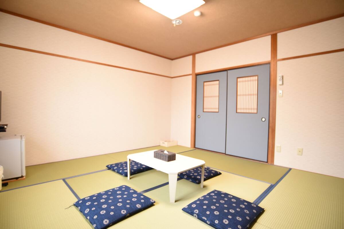 A tatami mat room with a low table and cushions, a sliding door, and a small cabinet.