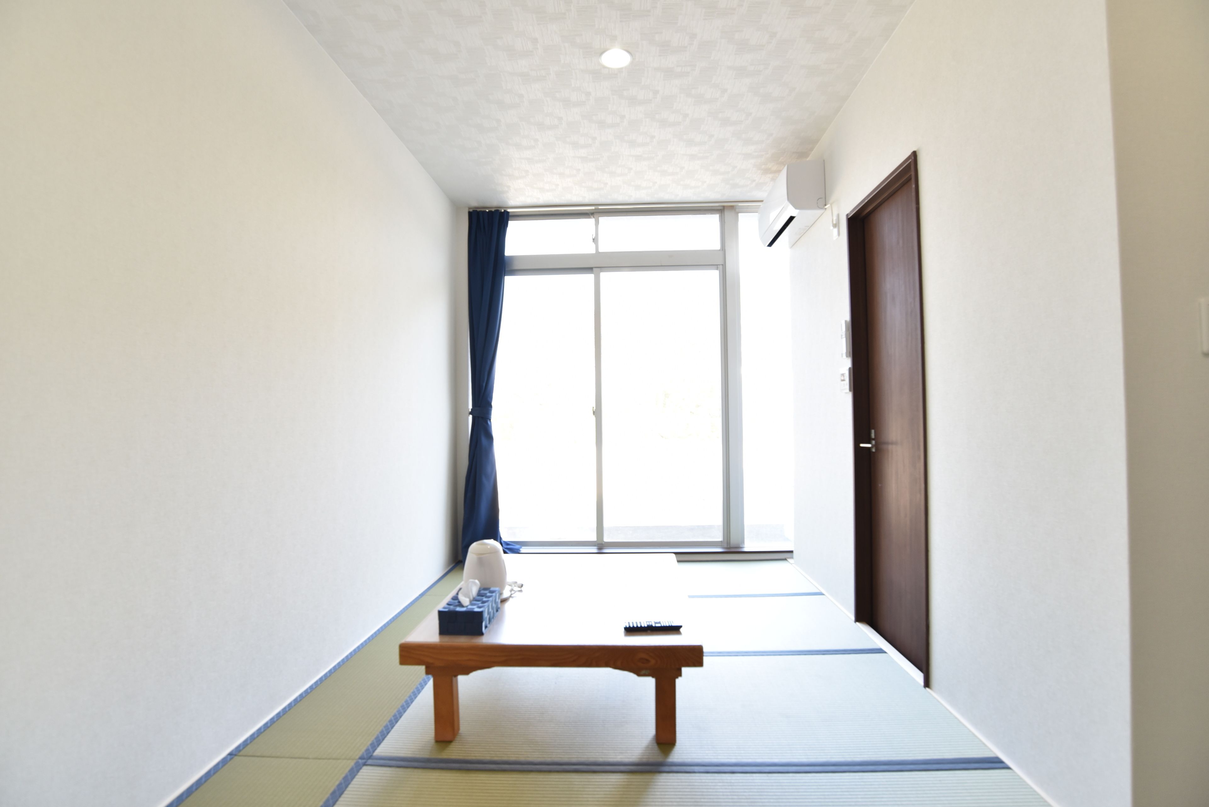 A hallway with tatami mats, a wooden bench, a sliding door, and a window with blue curtains.