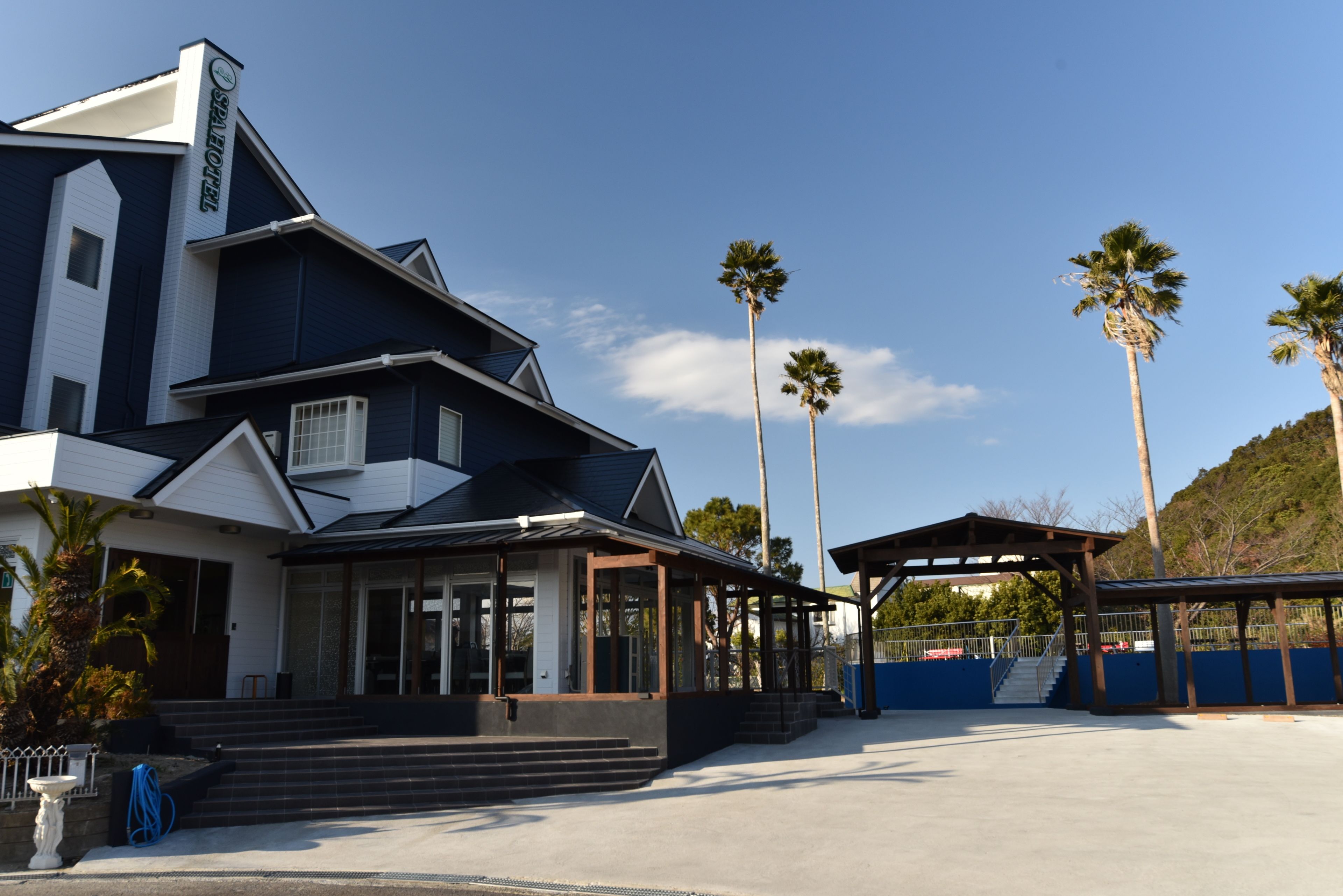 Un bâtiment moderne doté d’une entrée couverte et de palmiers en arrière-plan.