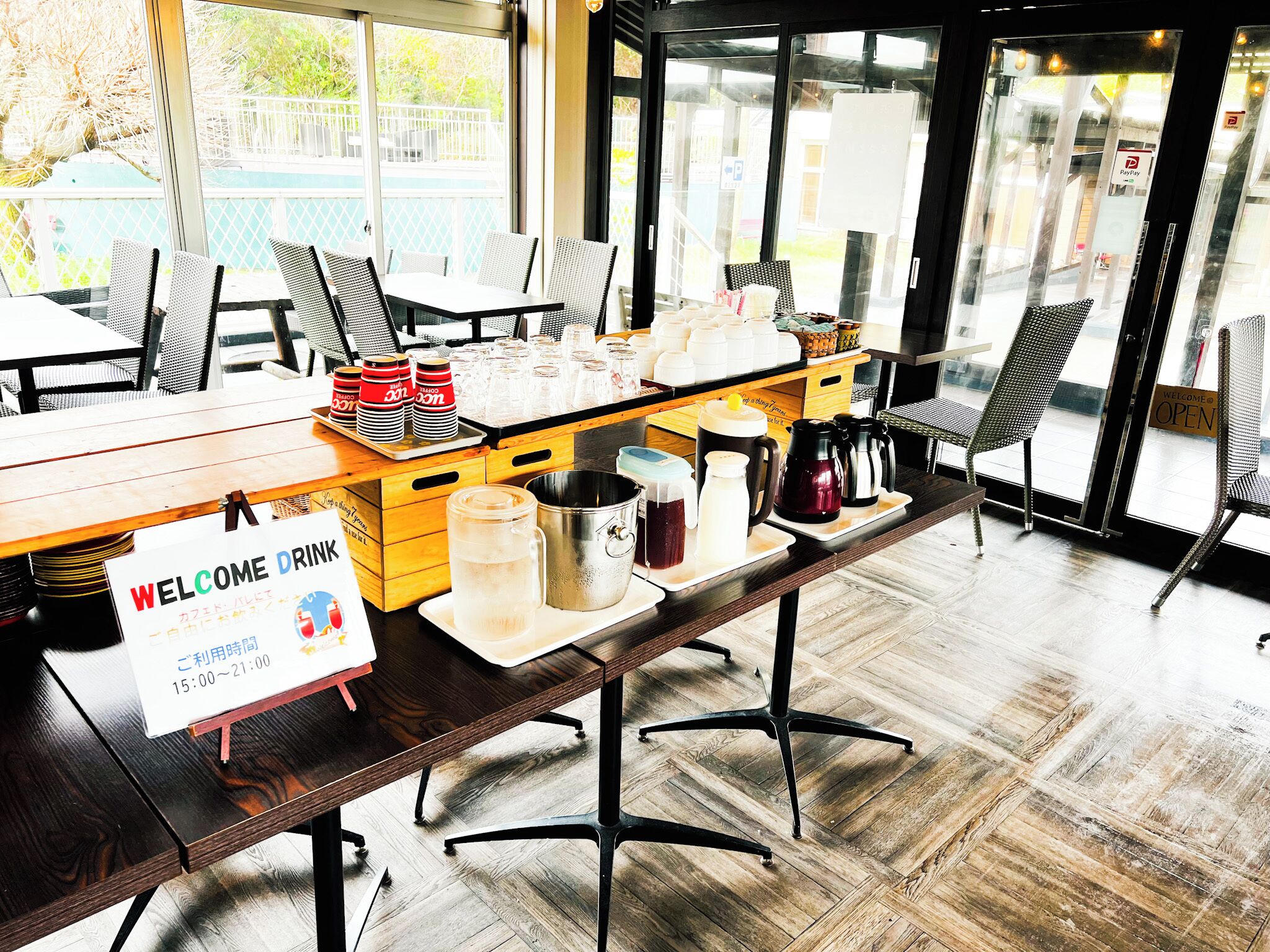 A reception area with a 'Welcome Drink' sign, a coffee station, and a view of the outside.