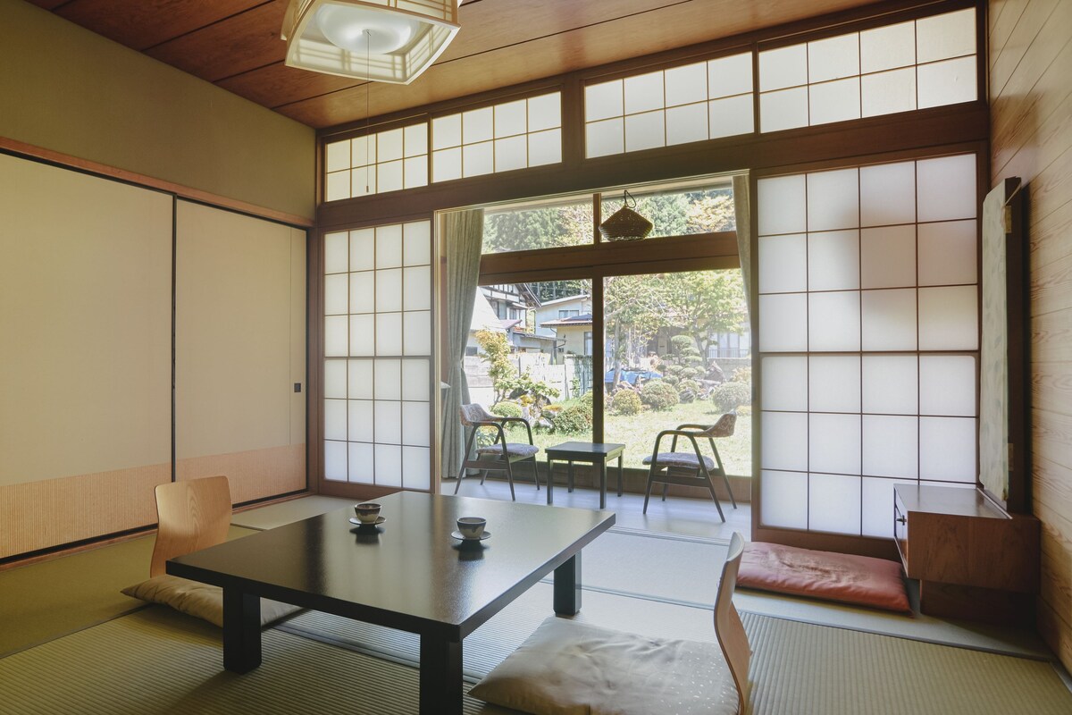 Una habitación japonesa tradicional con suelo de tatami, una mesita baja con cojín y puertas correderas shoji.