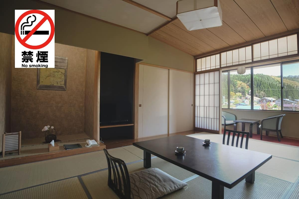 A traditional Japanese room with tatami flooring, a low table with cushions, a sliding door, and a view of a forested area.