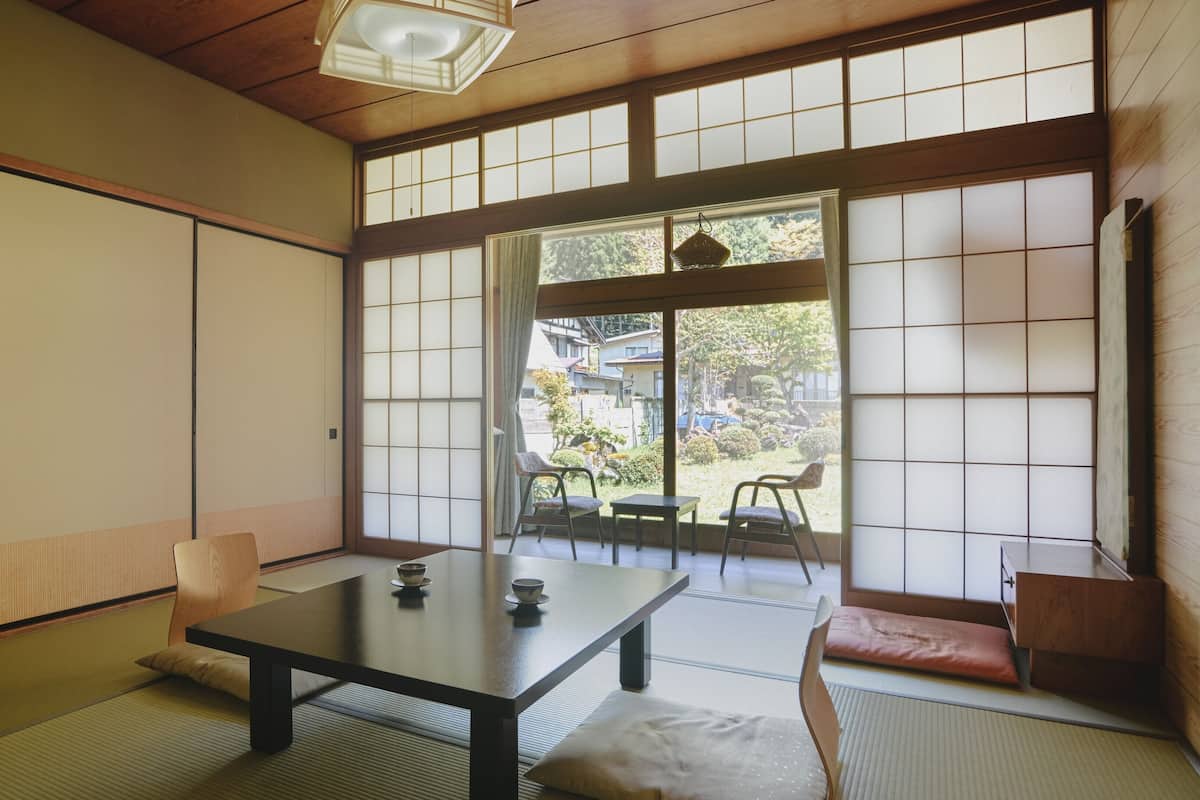 A traditional Japanese room with tatami flooring, a low table with a cushion, and sliding shoji doors.