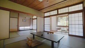 Ein traditioneller japanischer Raum mit Tatami-Boden, einem niedrigen Tisch, Schiebetüren und Blick durch große Fenster.
