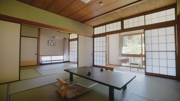 A traditional Japanese room with tatami flooring, a low table, sliding doors, and a view through large windows.
