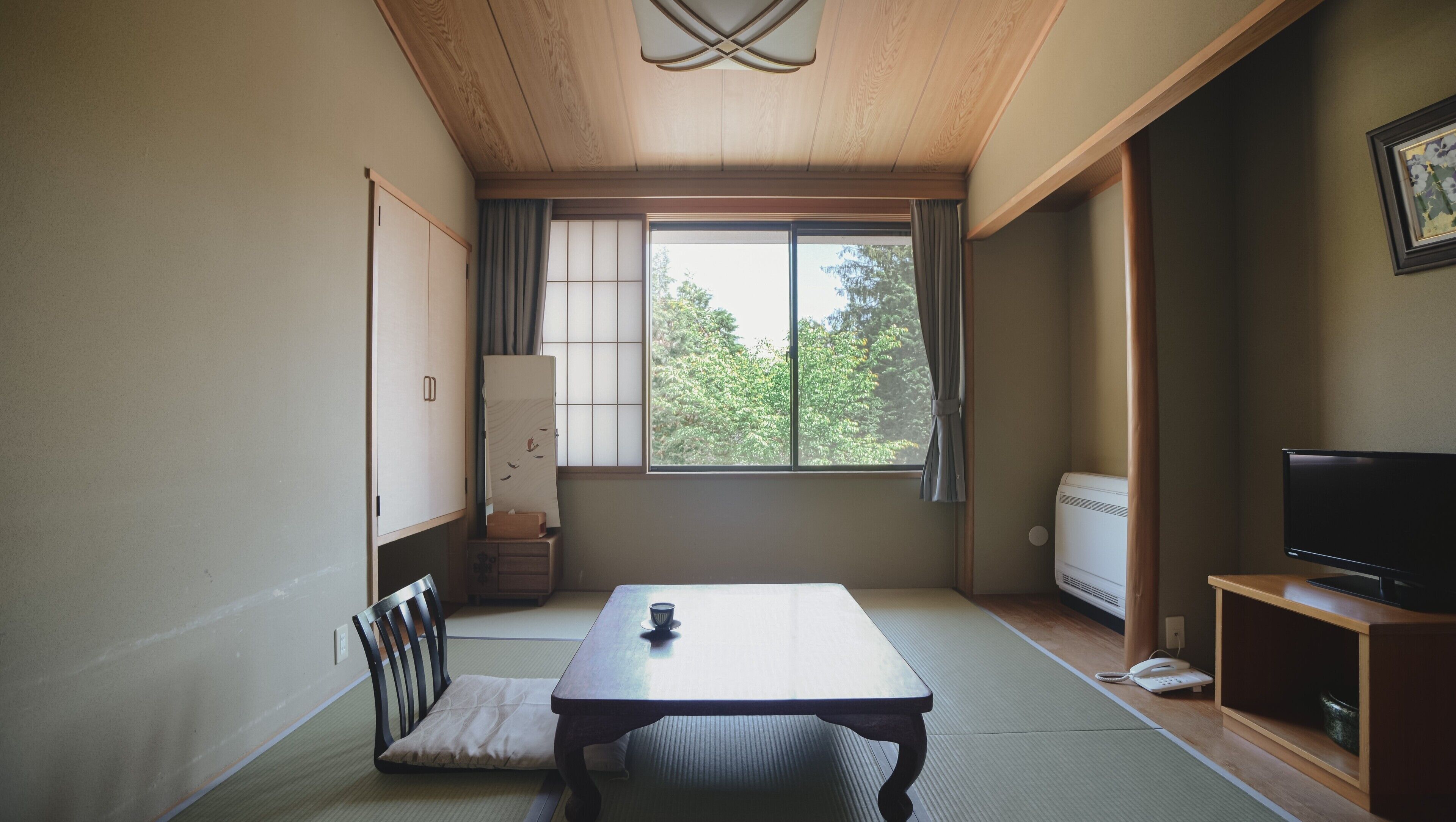A traditional Japanese room with tatami flooring, a low table, a chair, a television, and a sliding door.