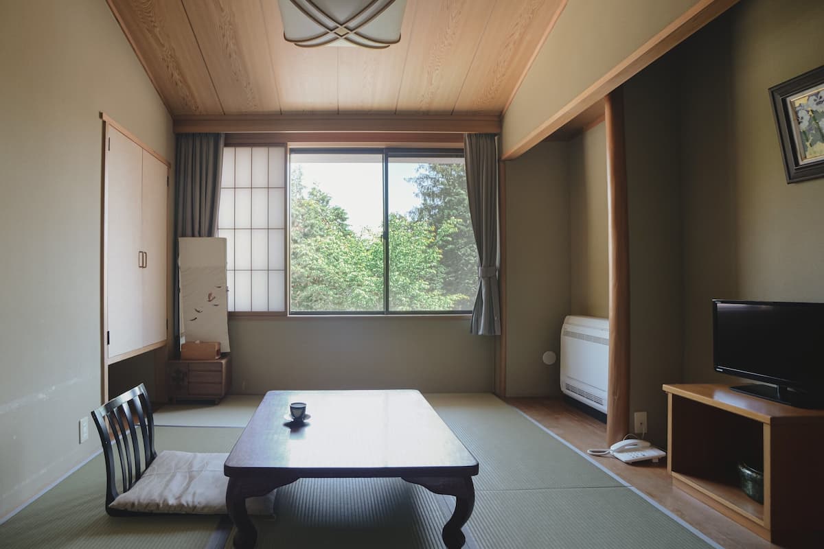 A traditional Japanese room with tatami flooring, a low table, a chair, a television, and a sliding door.