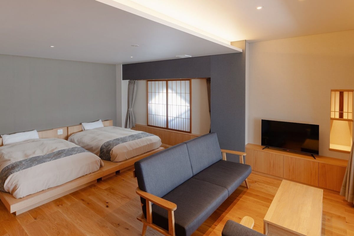 A hotel room with two beds, a sofa, a TV, and a small table.