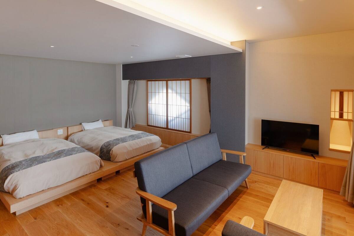 Habitación de hotel con dos camas, un sofá, un televisor y una pequeña mesa.