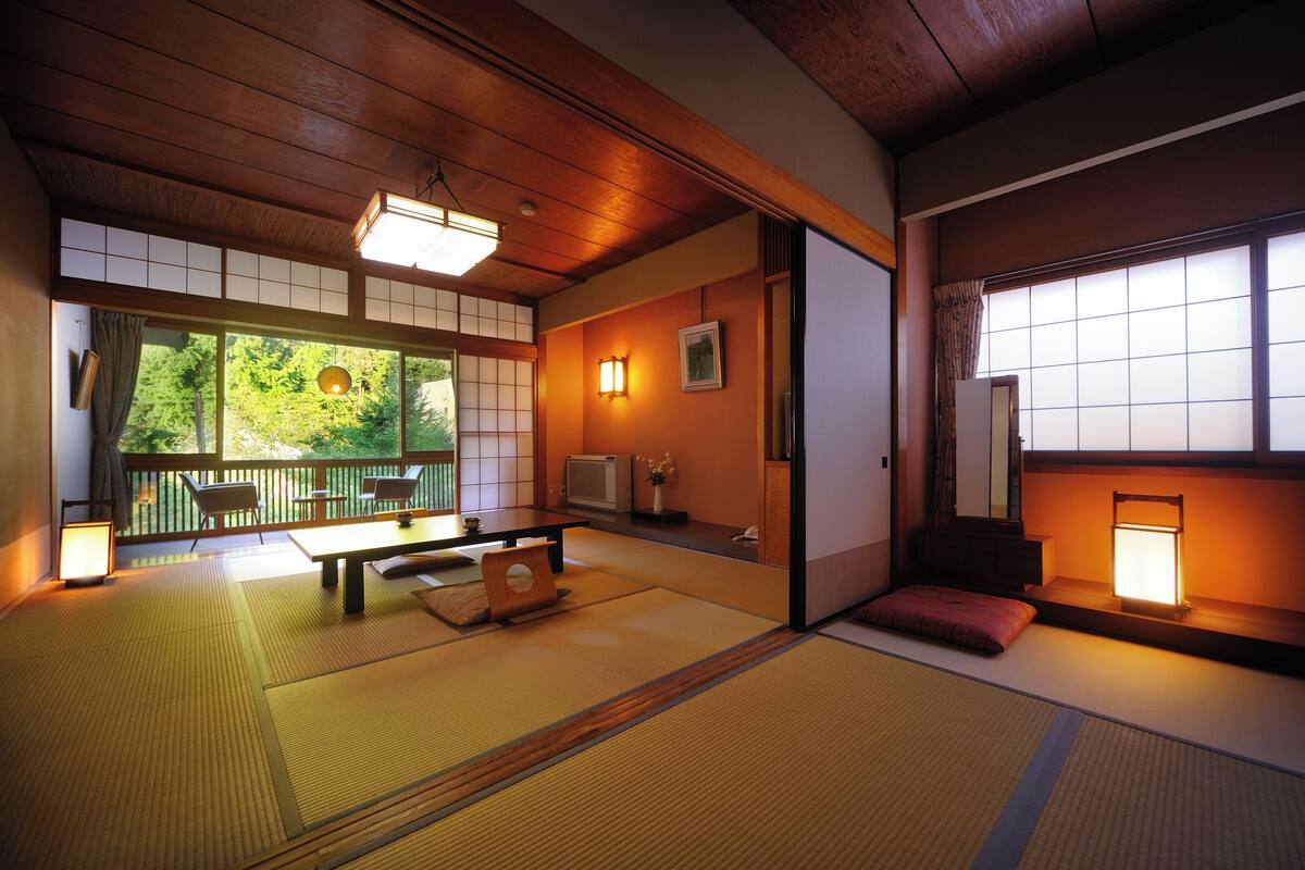 A traditional Japanese room with tatami flooring, a low table, chairs, a television, and sliding doors.