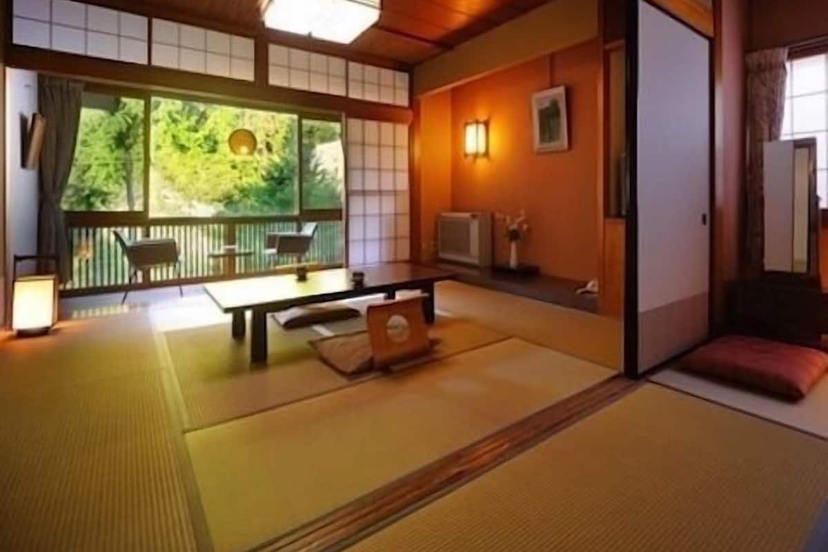 A traditional Japanese room with tatami flooring, a low table, a sofa, and a view of greenery outside.