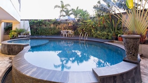 A circular pool with a stone border, surrounded by potted plants and a seating area with a table and chairs.