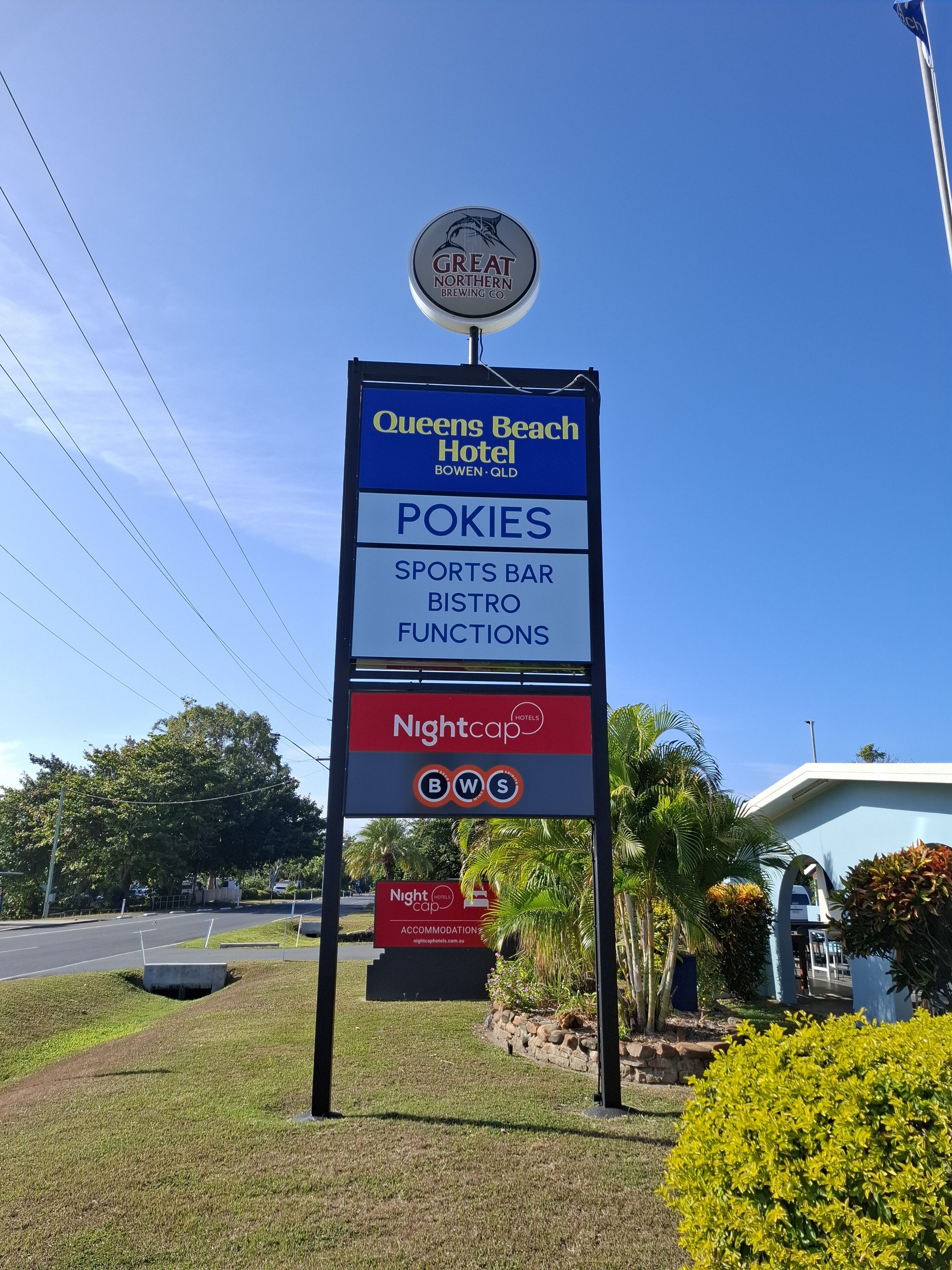 A sign for Queens Beach Hotel with amenities like Pokies, a sports bar, and a bistro.