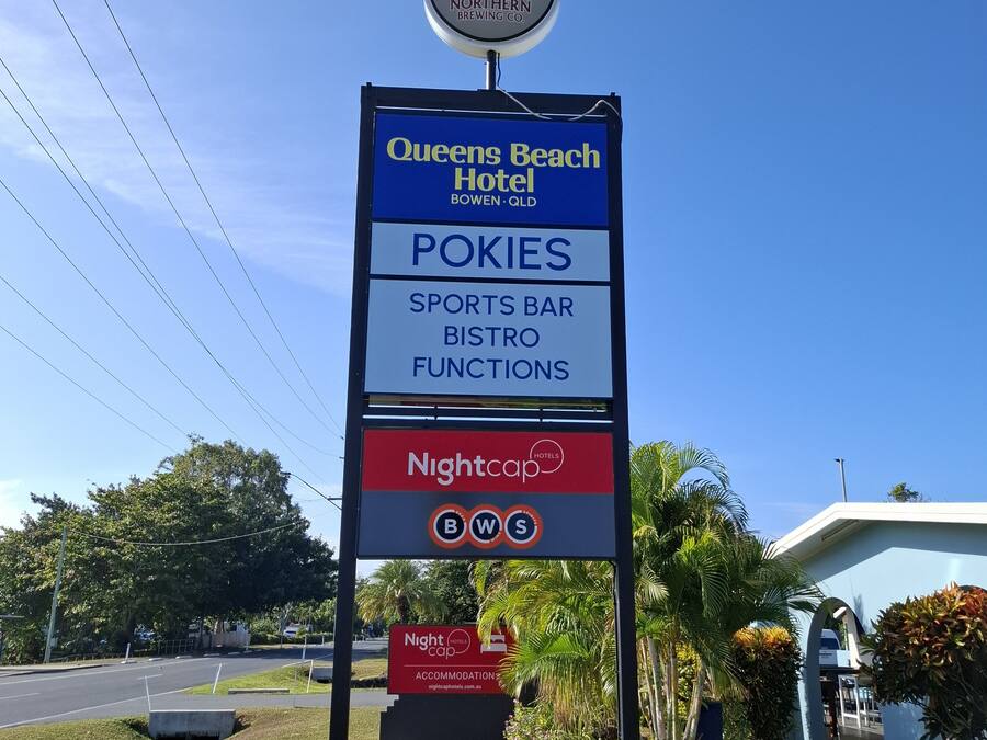 A sign for Queens Beach Hotel with amenities like Pokies, a sports bar, and a bistro.