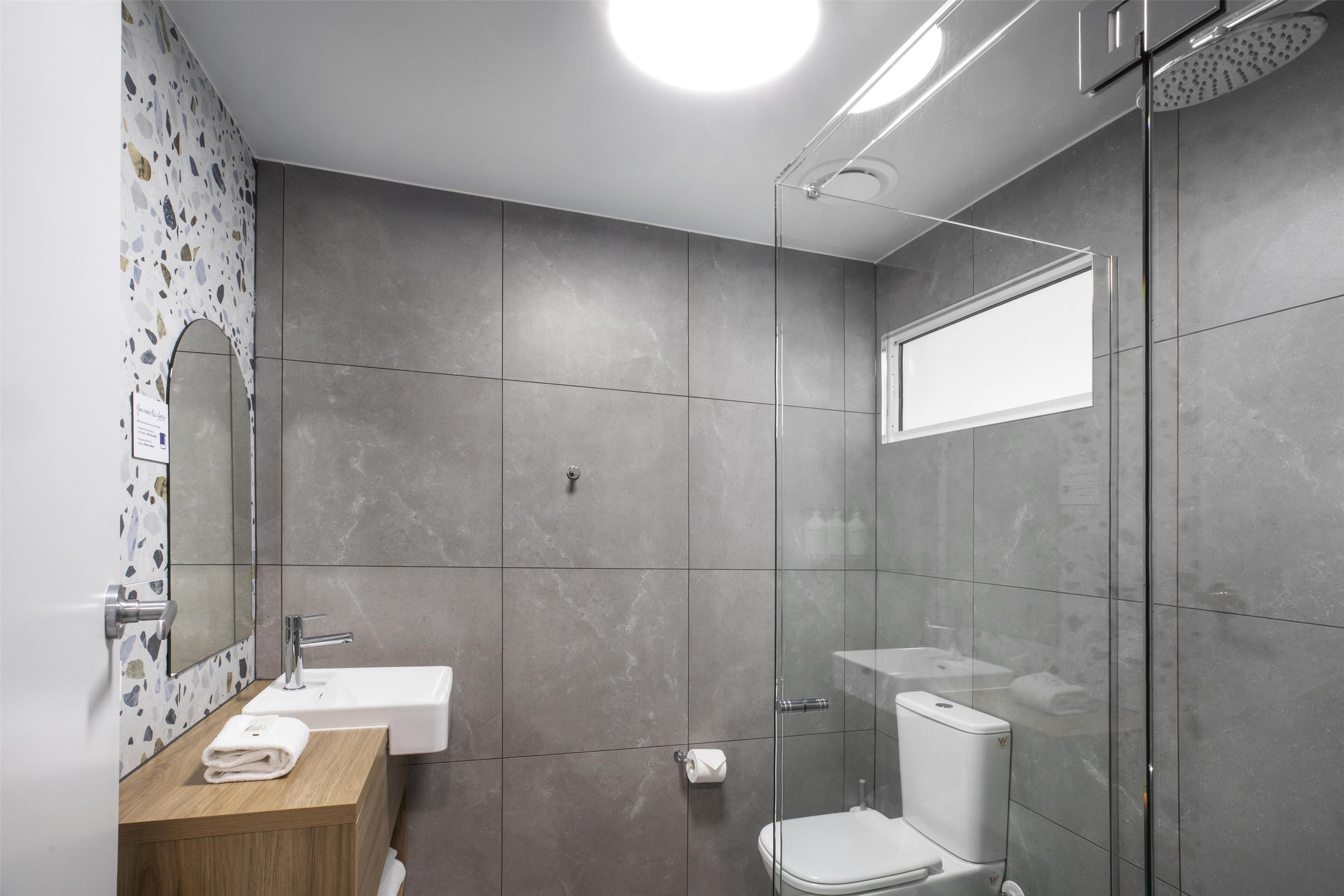 A modern bathroom with a glass shower enclosure, a wooden vanity with a sink, and a toilet.