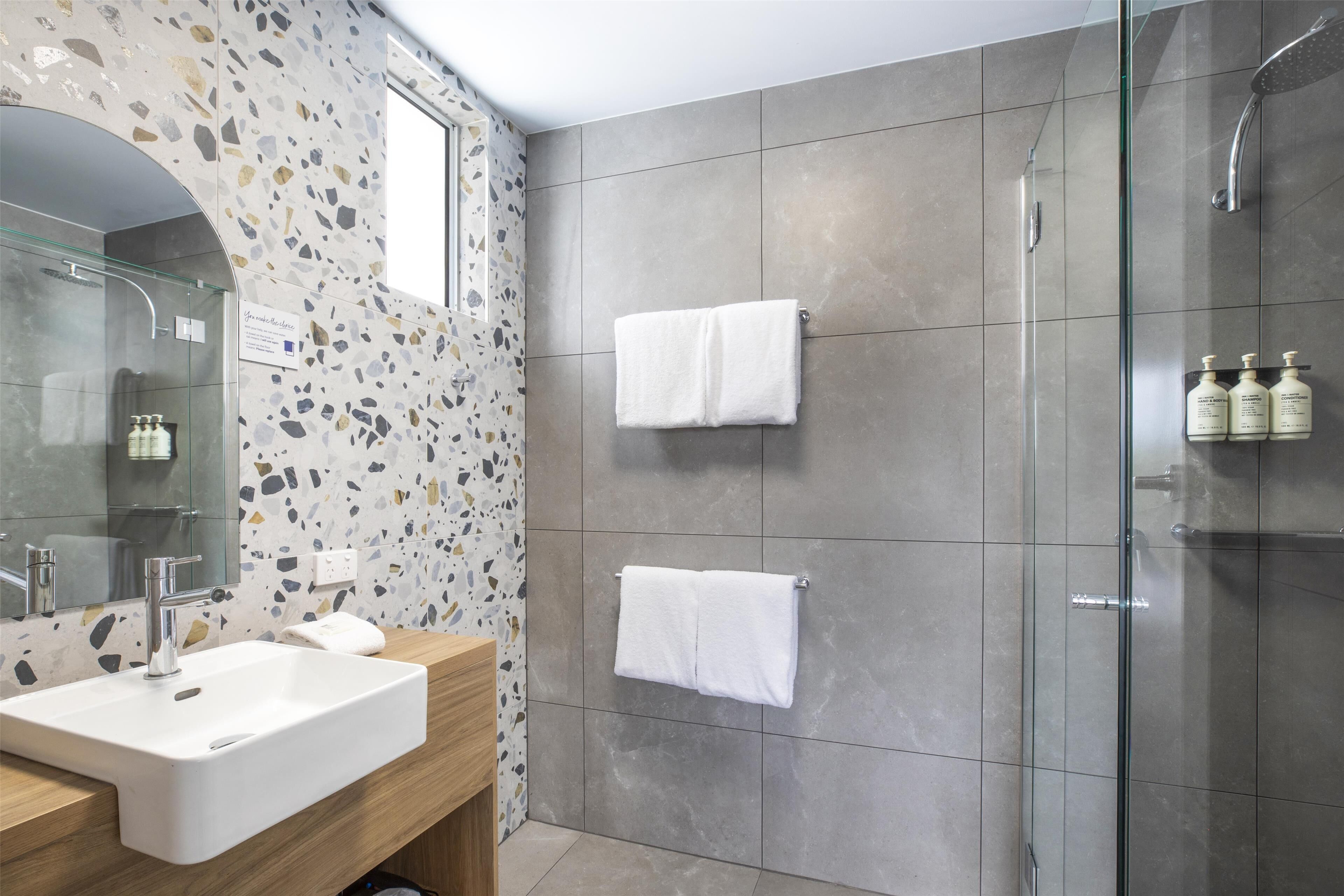 Un baño moderno con un lavamanos grande, cabina de ducha con mampara de vidrio y dos toallas colgadas en la pared.