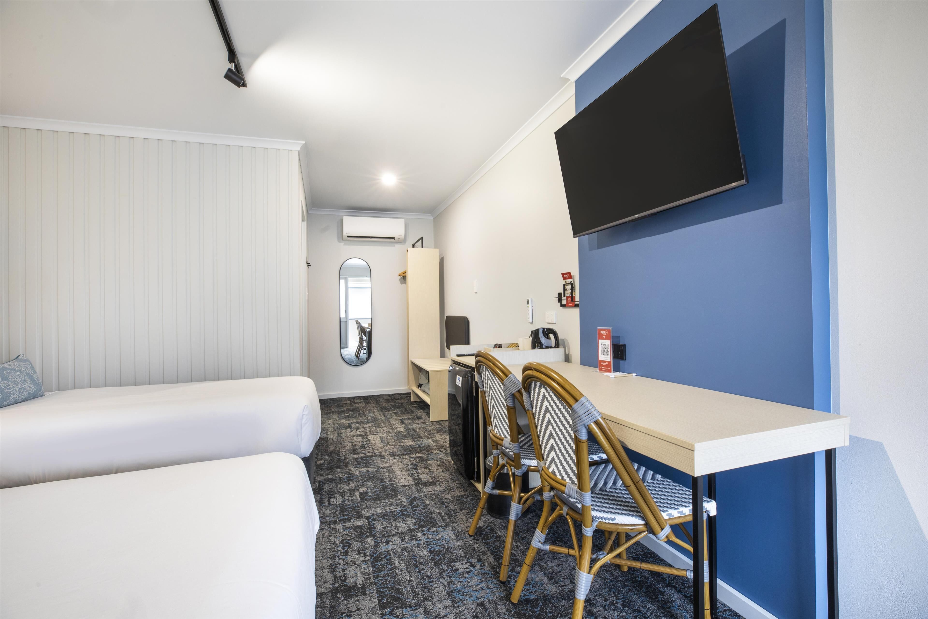 A hotel room with two beds, a desk, chairs, a TV, and a mirror.
