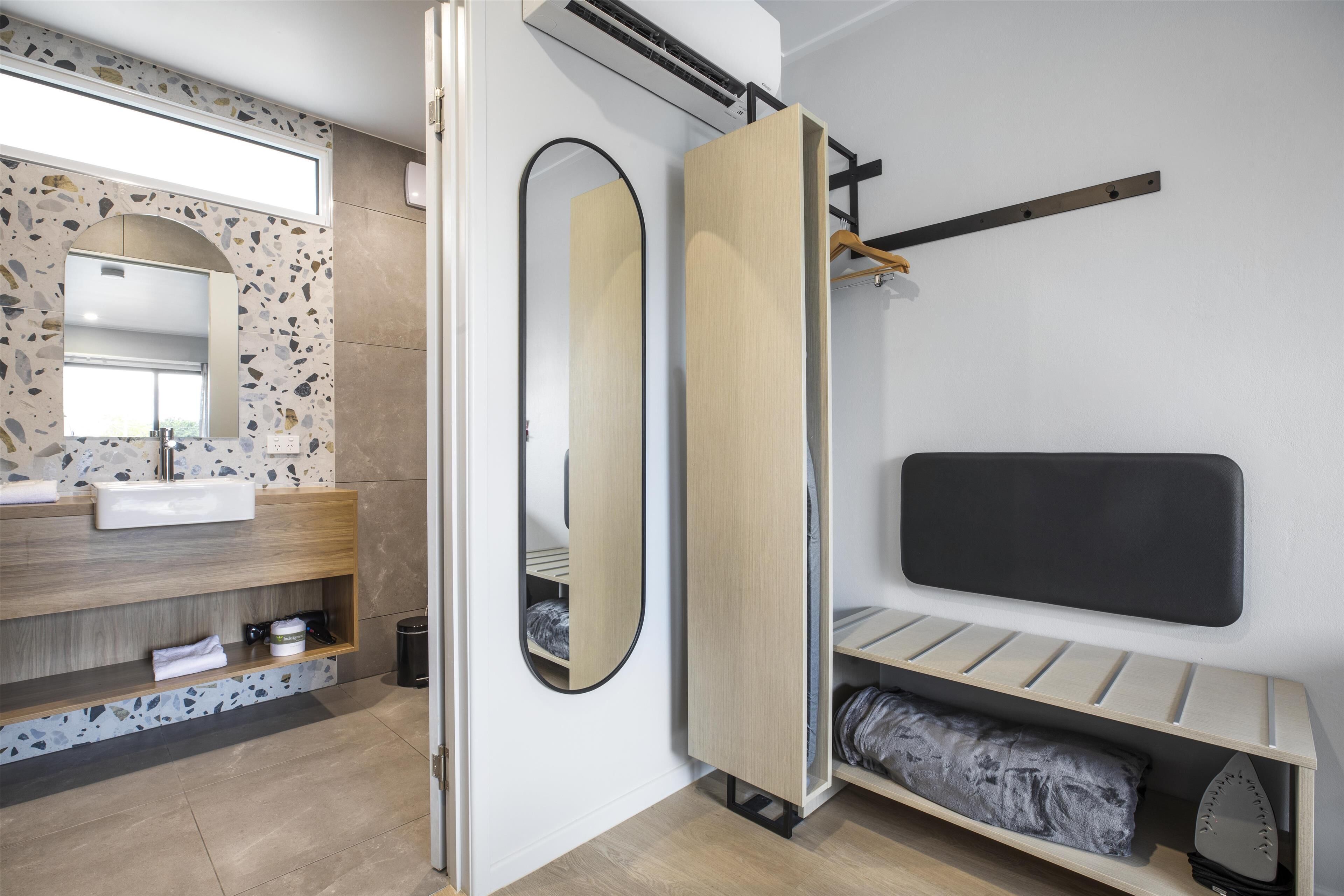 A modern bathroom with a freestanding mirror, a sink, and a built-in bench with storage.