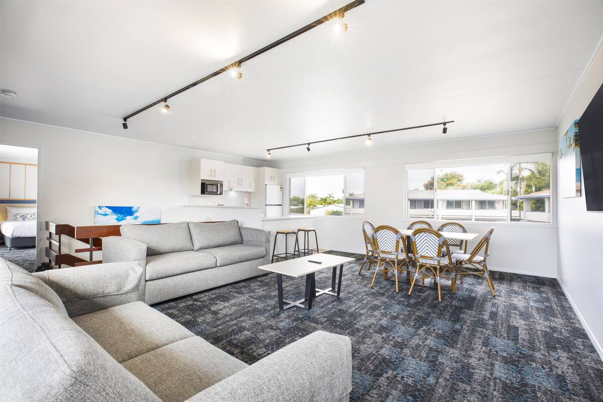 A modern living room with a grey sofa, a small table, and a dining area with wooden chairs.