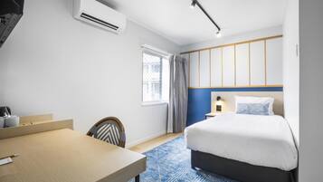 A hotel room with a bed, bedside table, chair, and a desk.