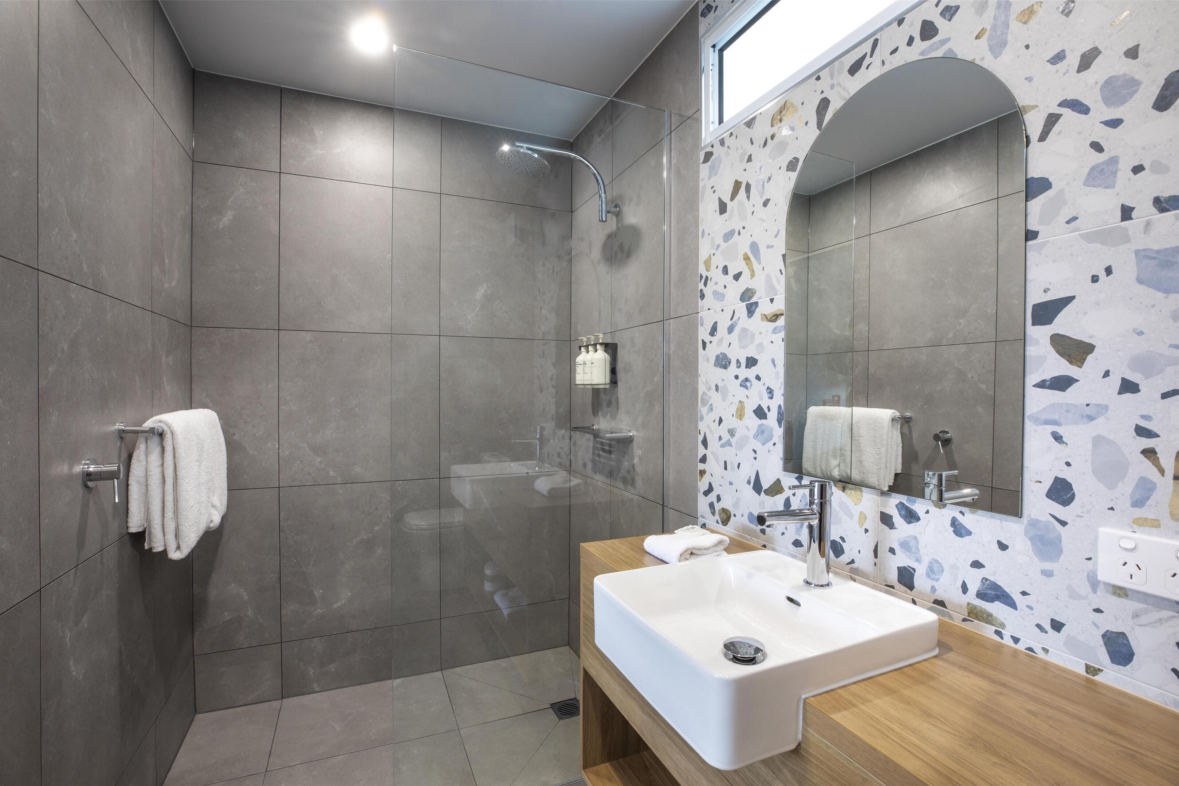 Un baño moderno con ducha, lavamanos y espejo.