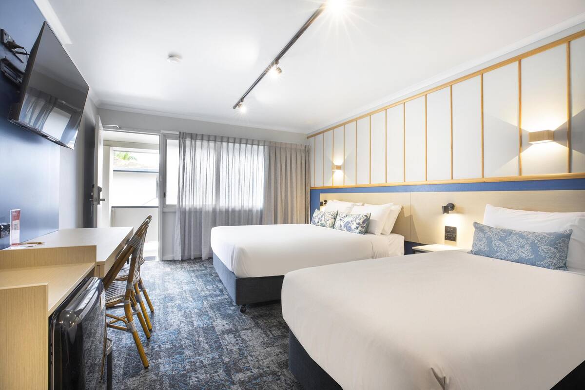 A hotel room with two beds, a desk, and a TV.