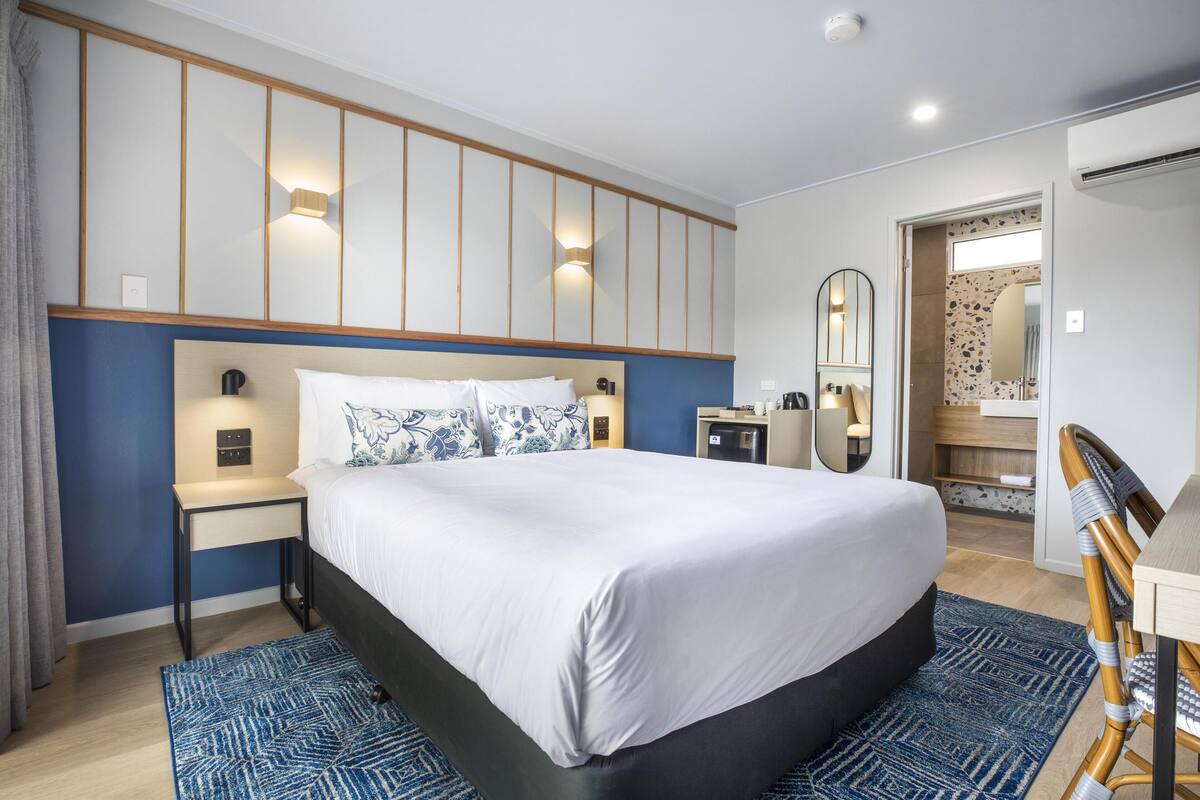 A modern hotel room with a large bed, bedside tables, a desk, and a mirror.