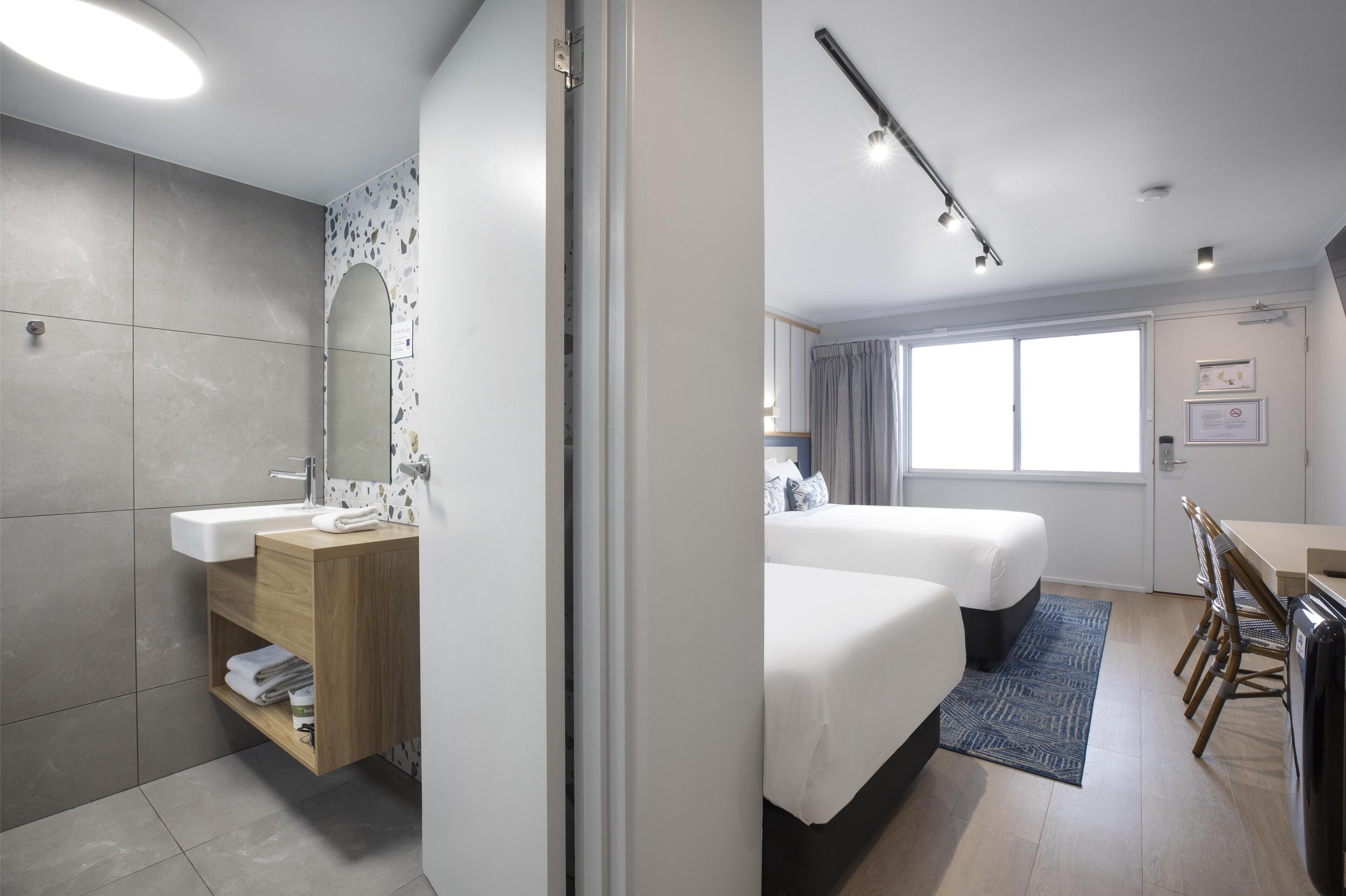 Habitació d'hotel moderna amb bany, llit, escriptori i zona de menjador.