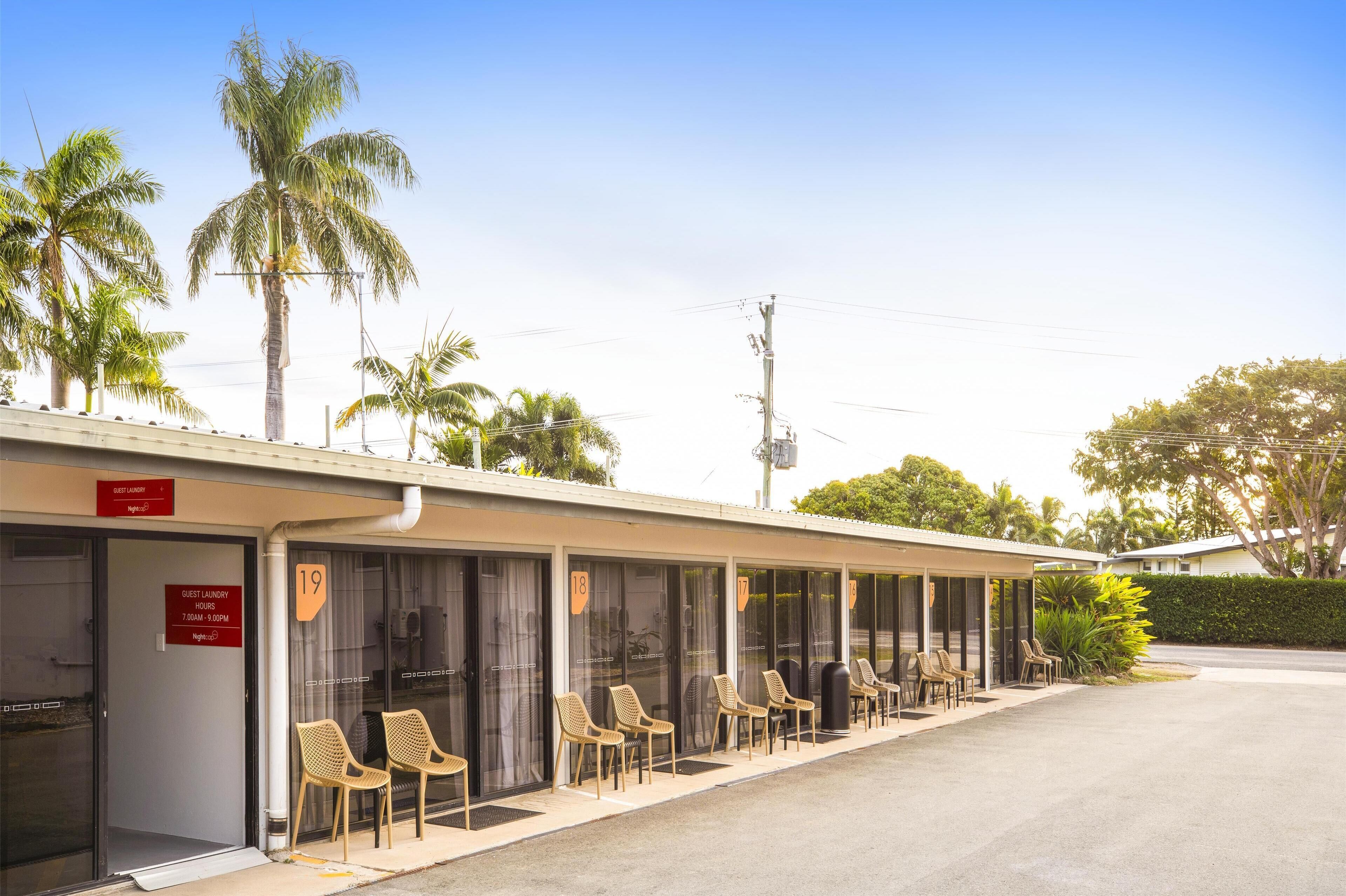 A motel with numbered guest rooms, outdoor seating, and palm trees.