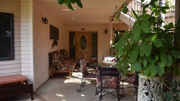 A covered porch with a dining table and chairs, a bench, and a door leading to the interior.