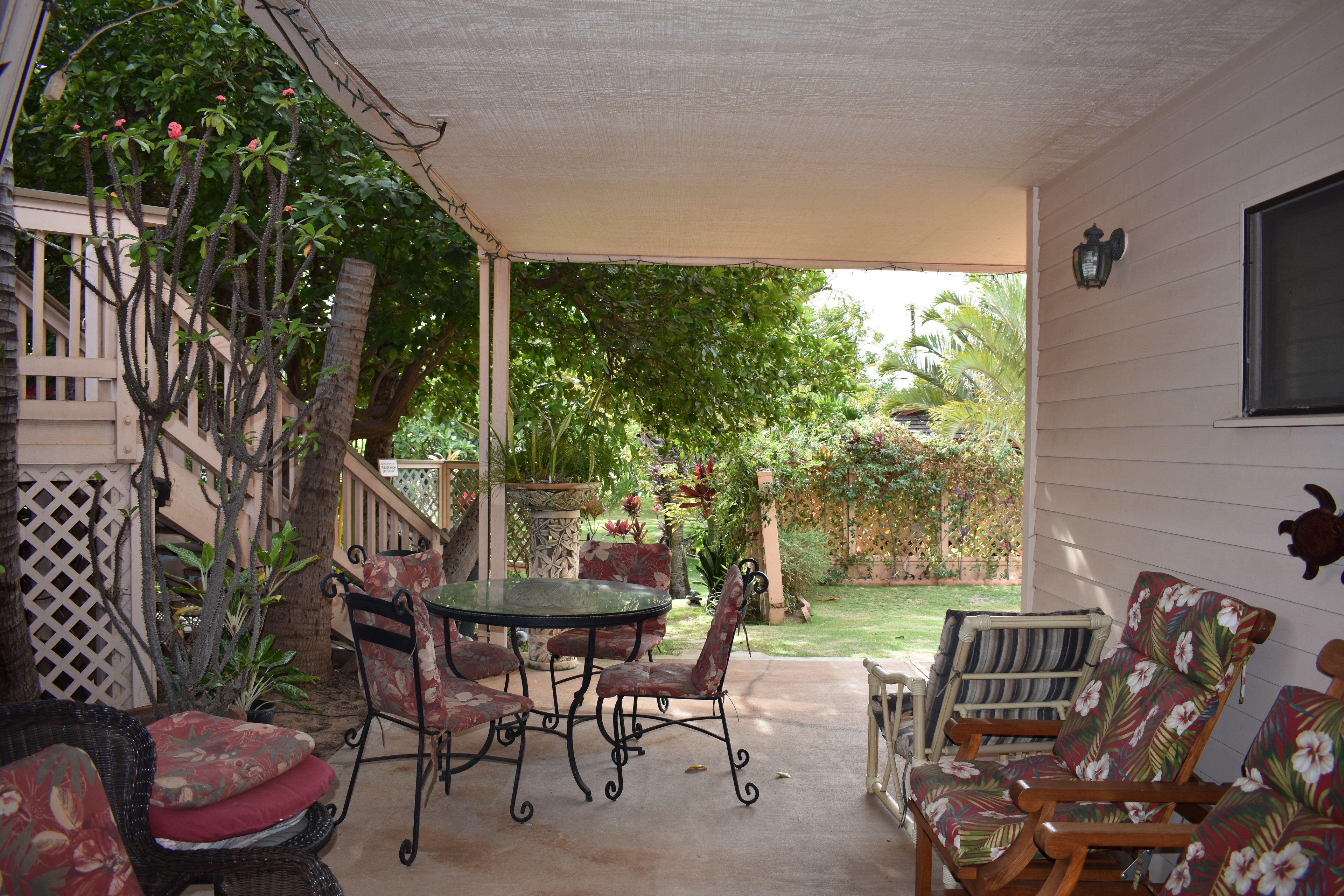 An outdoor patio with a table and chairs, surrounded by lush greenery and a wooden fence.