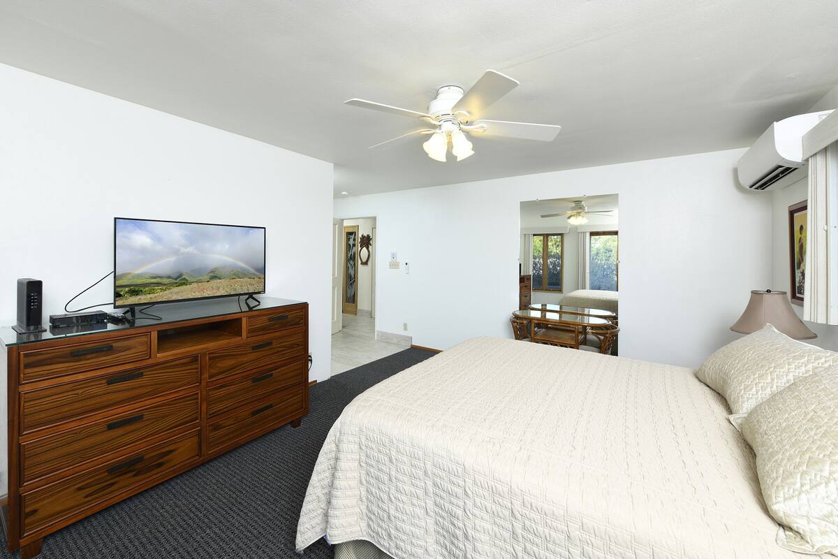 A bedroom with a bed, a wooden dresser, a television, and a ceiling fan.