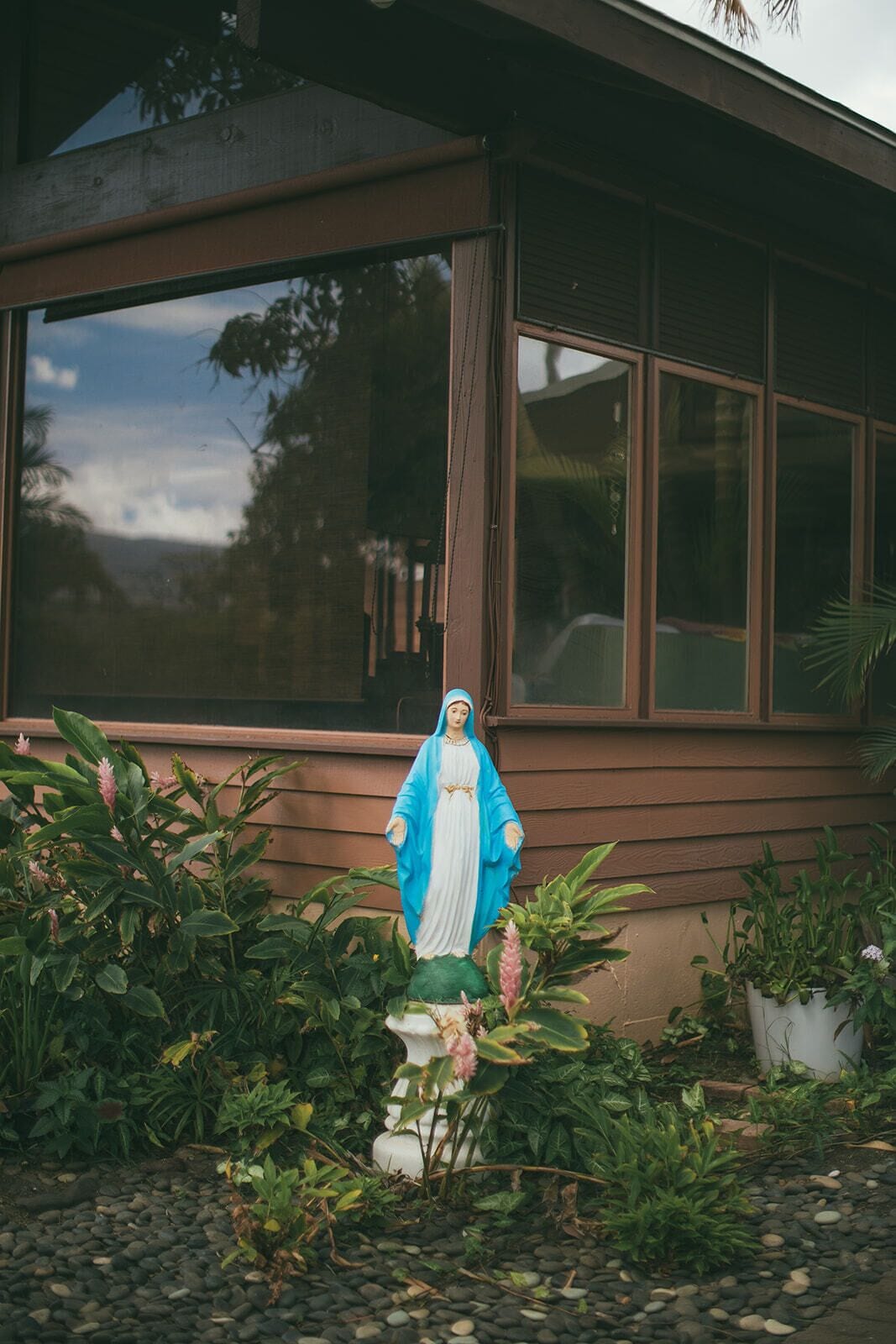 Una estatua de una figura religiosa en un jardín, con una casa al fondo.