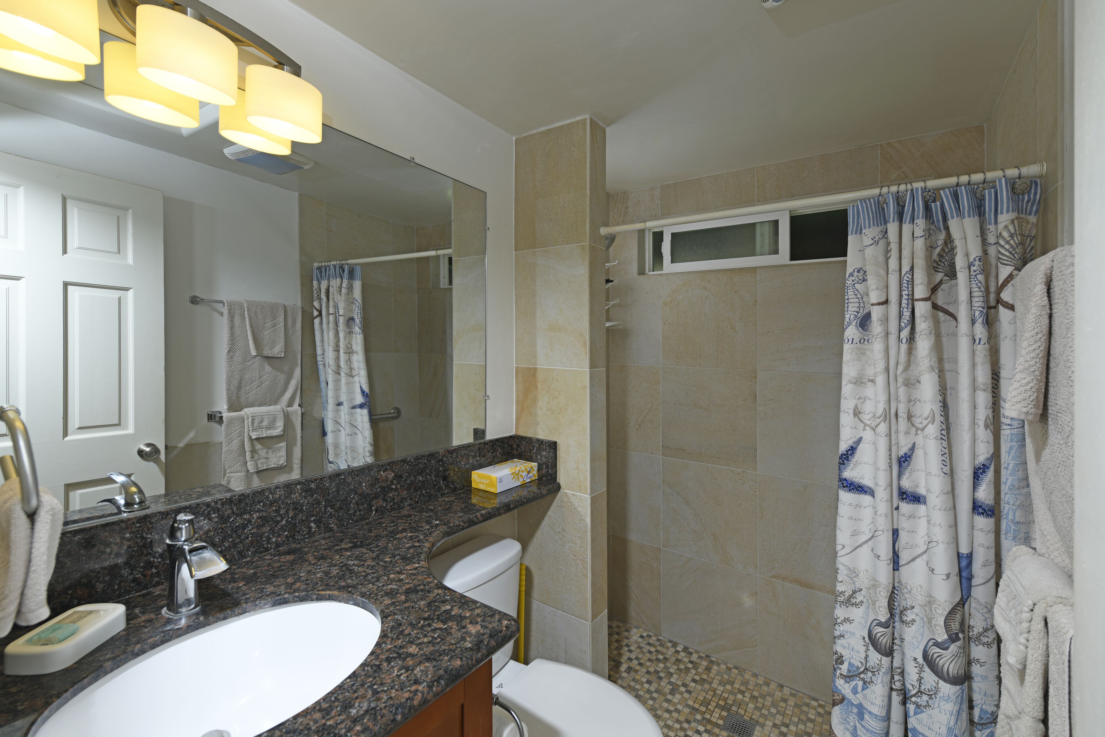 A bathroom with a granite countertop sink, a mirror, a shower curtain with a nautical theme, and a towel rack.