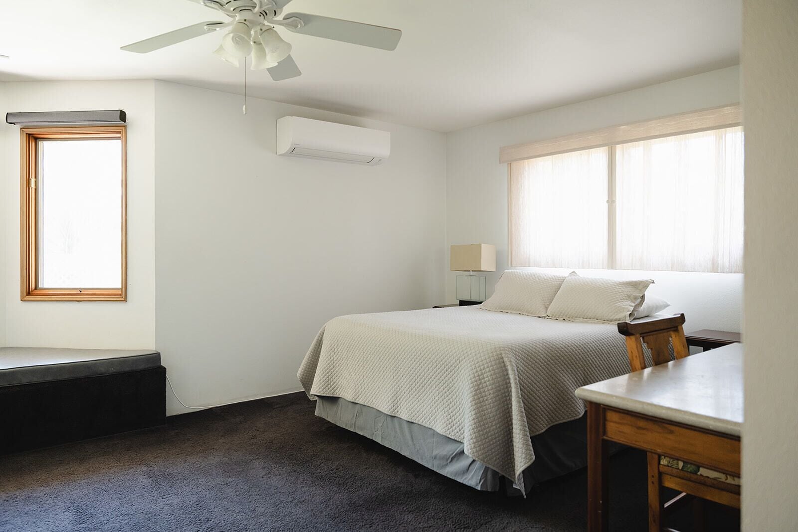 A bedroom with a bed, a desk, a chair, a ceiling fan, an air conditioning unit, and a window with curtains.